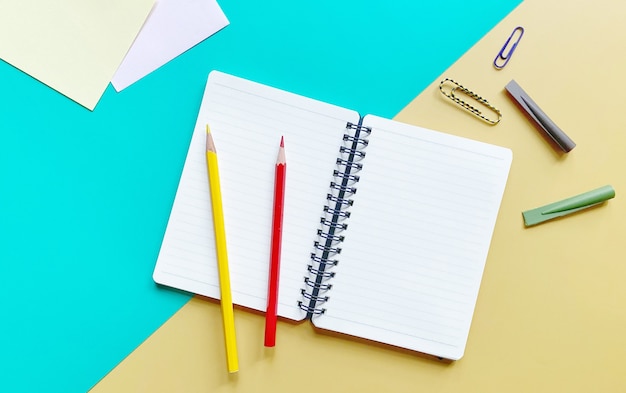 Top view flat lay of notebook with colored pencils paper clips and pencil caps on green and yellow