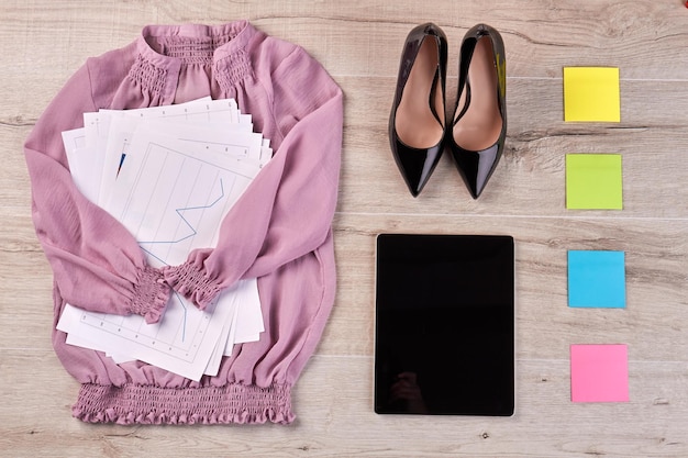 Top view flat lay pink blouse with work papers and shoes tablet with sticky notes on the desk