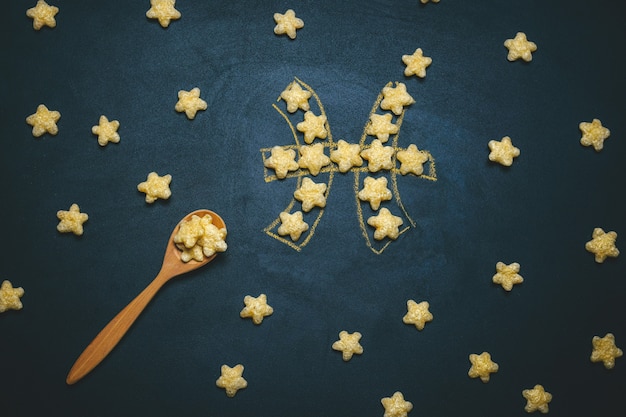 Top view flat lay Pisces, horoscope sign made from crispy corn stars on a black