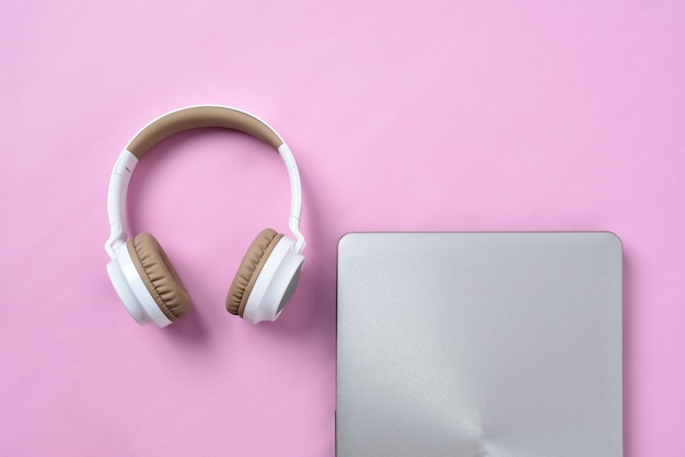 Top View Flatlay of modern wireless headphone and minimalist laptop on pink color workspace