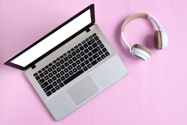 Top View Flatlay of modern wireless headphone and minimalist laptop with white screen on pink color workspace