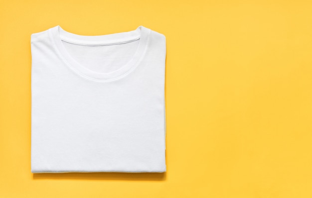 Top view of folded white color t-shirt on yellow background