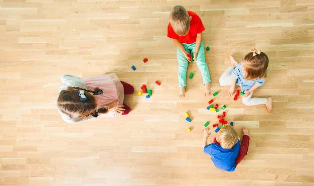 Photo top view of four lovely kids playing on a floor constructing of wooden blocks. portrait of children sitting bare feet playing in calm cooperation