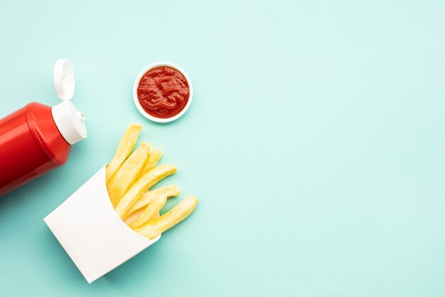 Top view of french fried in box with bottle of tomato sauce on color table