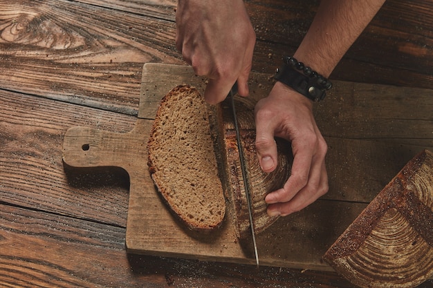 Top view of fresh bread cut into a man's hands on a wooden boardin the background