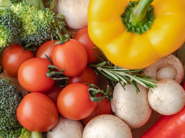 Top view of fresh cherry tomatoes yellow pepper mushrooms and broccoli on the table Mixed vegetables