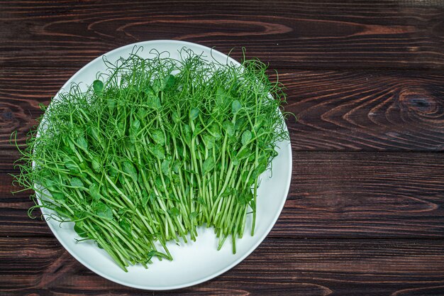 Top view of fresh chopped pea microgreen sprouts on plate on wooden surface