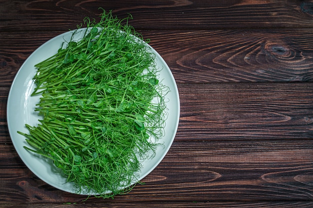 Top view of fresh chopped pea microgreen sprouts on plate on wooden surface