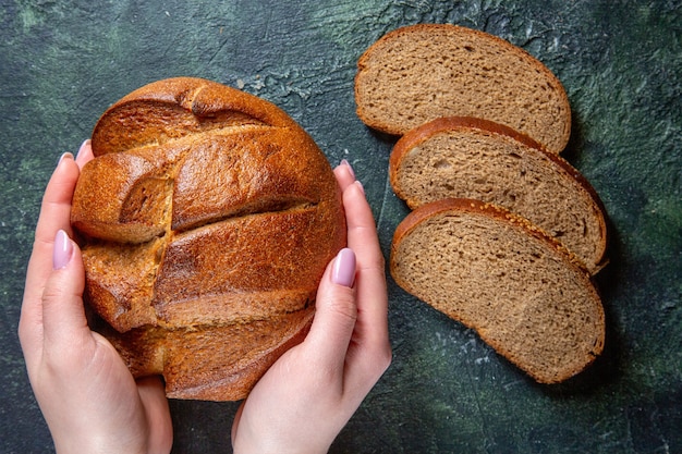 Top view fresh dark bread with female hands on dark desk