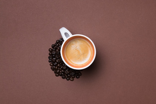 Top view of a fresh espresso cup surrounded by coffee beans on brown surface