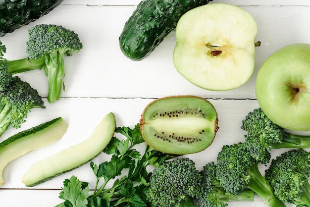 Top view of fresh green fruits and vegetables on white wooden surface