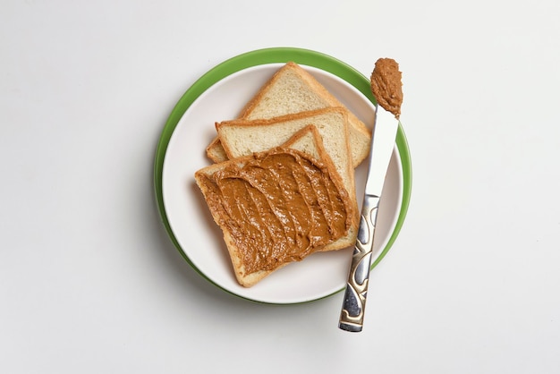 Top view of fresh toasts on the plate buttered with tasty peanut butter on the white surface