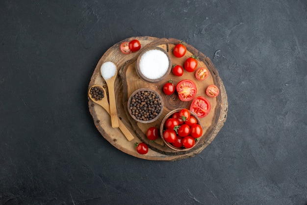 Top view of fresh tomatoes and spices on wooden board on black surface