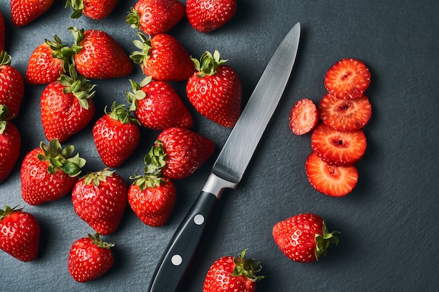 Top view of freshly cut red strawberries with a knife on dark