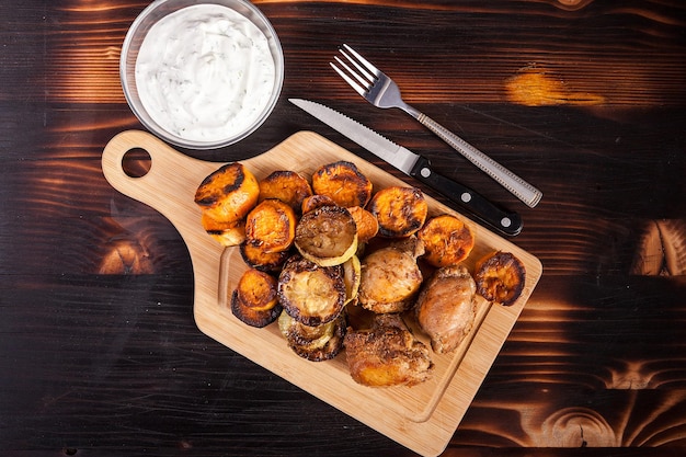 Top view of fried chicken next to grilled sweet potatoes, quash and sour cream souce on wooden background