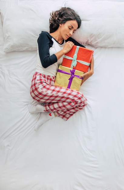 Top view full-length photo of a beautiful young curly brunette woman in casual clothes with gift boxes in hands. Dreaming and relaxing