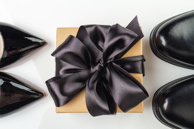 Top view of gift box with black ribbon and shoes classic mens and womens footwear isolated on white