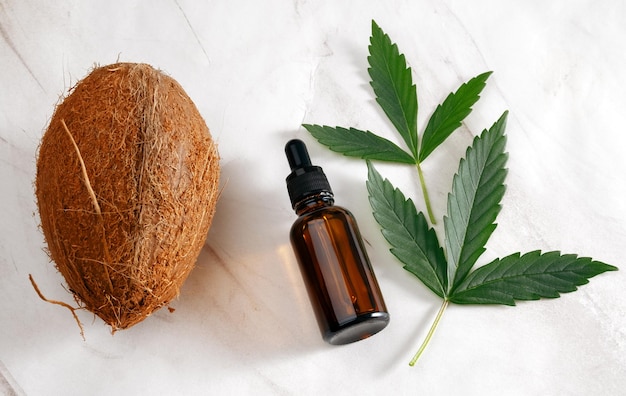 Top view glass bottle coconut and marijuana leaves flat lay on marble background