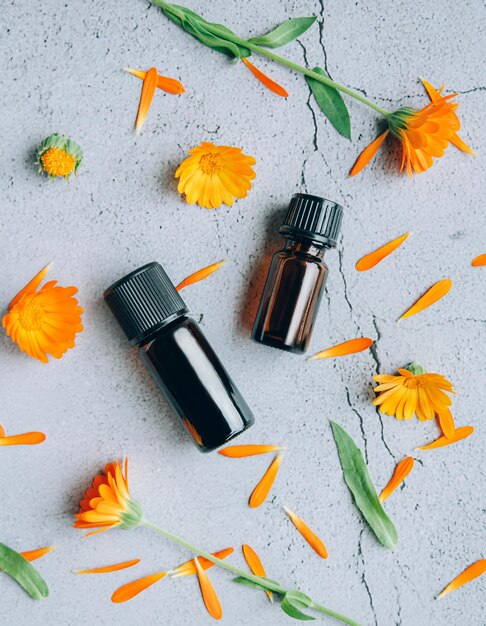 Photo top view of glass bottles of calendula essential oil with fresh marigold orange yellow flowers