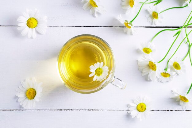 Top view of a glass cup of chamomile tea and chamomile flowers