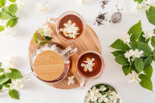 Top view of glass cups and teapot with jasmine tea and jasmine flowers on a round wooden board white background