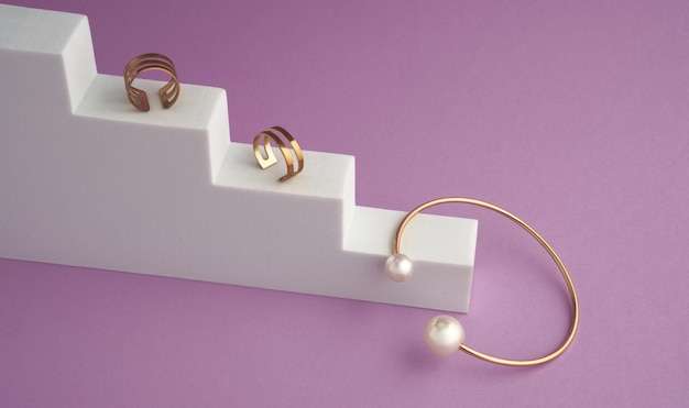 Top view of Gold with pearls bracelet and rings on white podium on violet color background with copy space