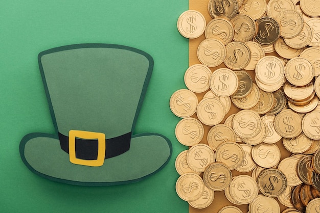 Top view of golden coins with dollar signs and paper hat on green and orange background st patrick