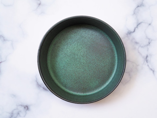 Top view of green ceramic plate glazed tile, pottery bowl, empty dish isolated on white marble table.