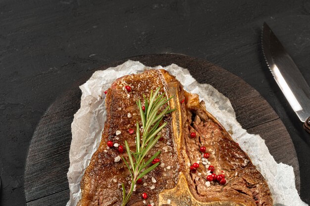 Photo top view of grilled t-bone steak with spices on black table