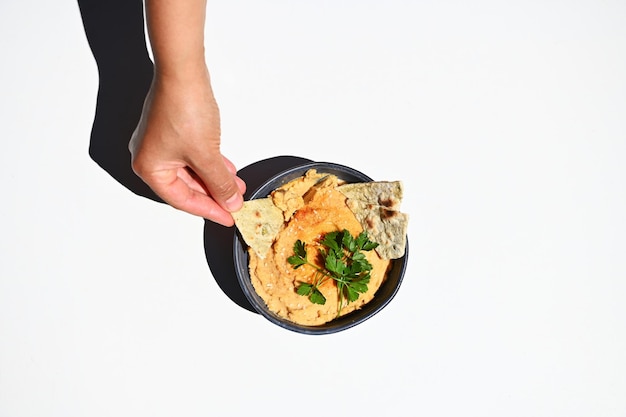 Top view of a hand dipping pita bread into a creamy consistency vegan dish oriental hummus with parsley in a bowl