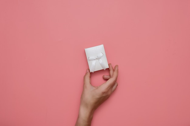 TOp view hand with white box with bow on punk surface. 