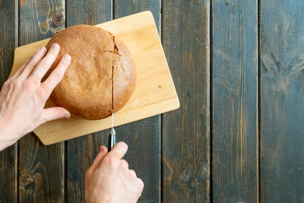 Top view of hands cuttingresh baked bread on wooden surface