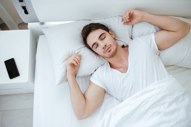 Top view of handsome young man in white t-shirt sleeping in bed