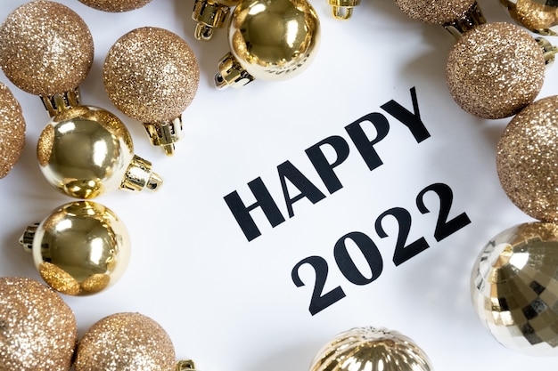 Top view of Happy 2022 message surrounded by golden Christmas balls, white background and copy space.