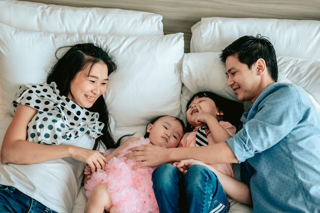 Top view of happy family is having fun in bedroom Enjoying being together Parents are tickling their little baby while lying in bedWeekend activity happy family lifestyle concept