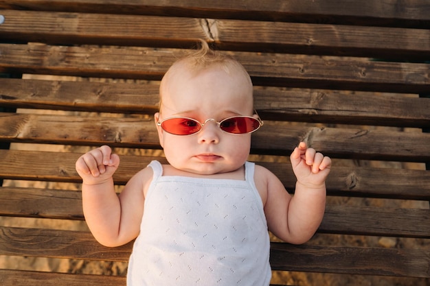 Top view of a happy little boy with glasses lying on a wooden sunbed