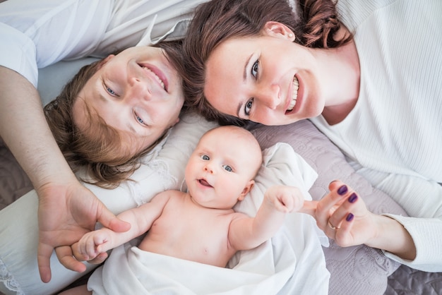 Top view happy positive Young family husband wife and little newborn baby lie on a cozy bed