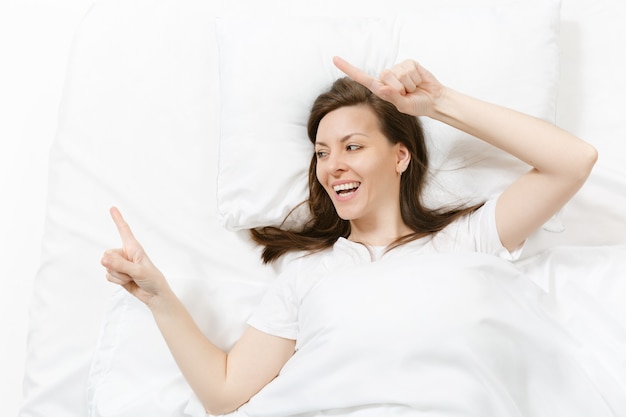 Top view of head happy brunette young woman lying in bed with white sheet, pillow, blanket