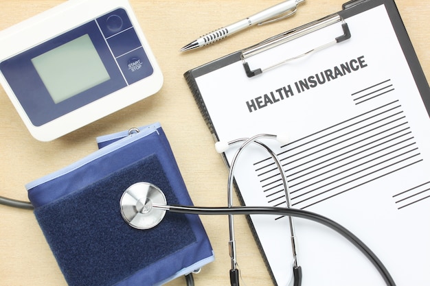 Top view health insurance form and pulse gauge with stethoscope on wooden background. 