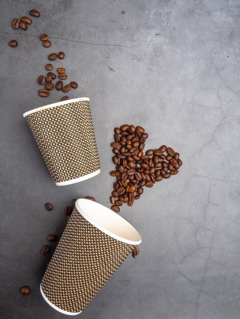 Top view heart of coffee beans and paper disposable cups flat lay concrete background mock up blank paper cups