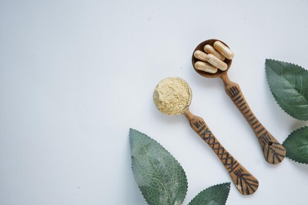 Top view of herbal medicine capsule and powder on wooden spoon on white