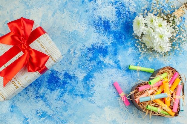 top view holiday gift scroll wish papers in heart shaped box flowers on blue background with free space