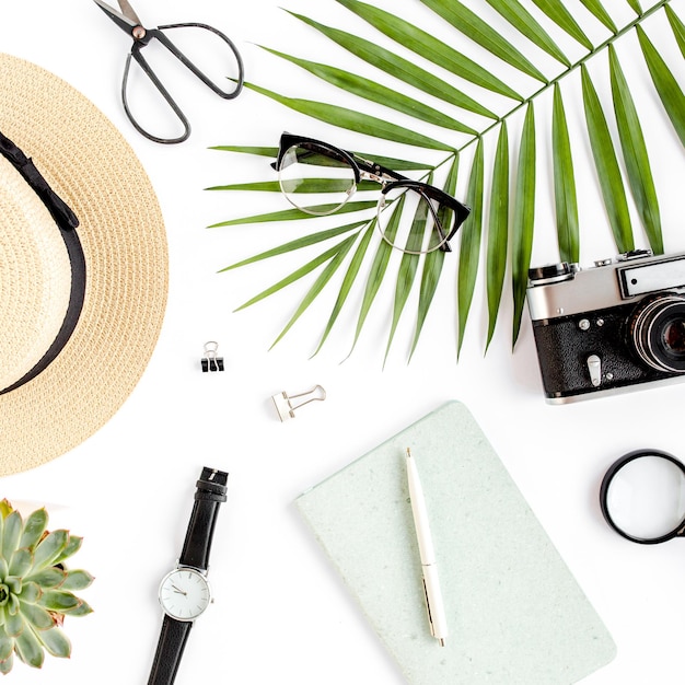 Top view home office desk workspace with straw hat glasses retro camera notepad and tropical palm le