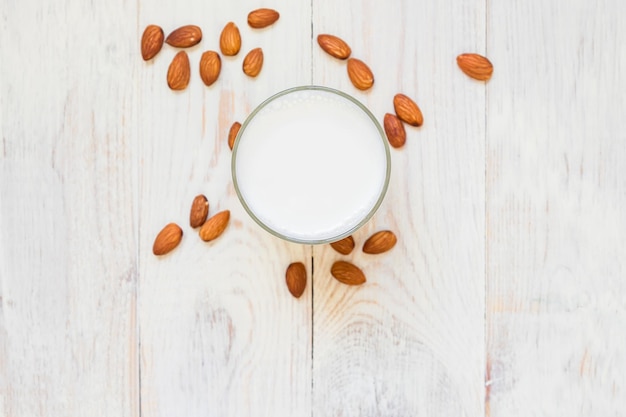 top view of Homemade Almond milk in a glass and scattered nuts on wooden background copy space