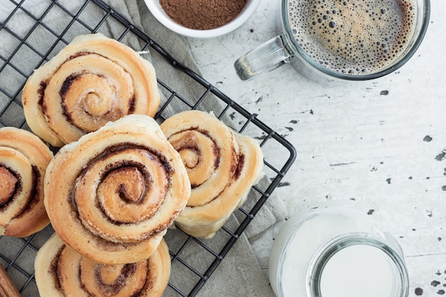 Photo top view of homemade cinnamon rolls on grill danishes and american coffee in glass cup.