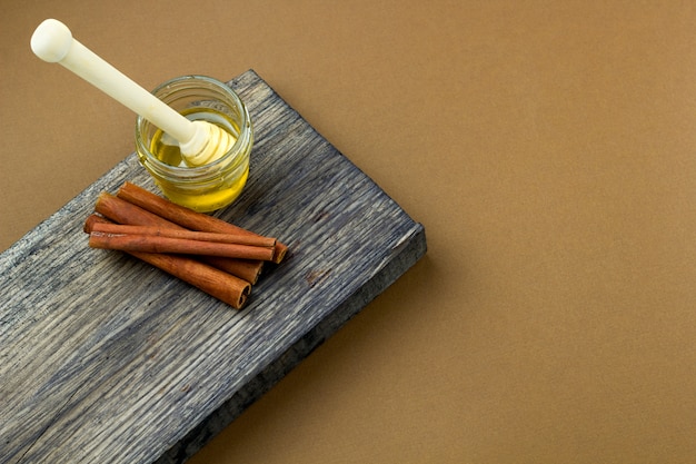 Top view honey jar and cinnamon on a wooden board brown background copy space