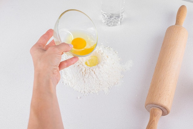 Top view of how puts egg in mound the flour rolling pin on white background Kneading the dough