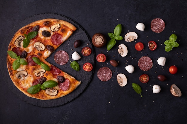 Top view of hungry pizza eating mozzarella cheese, mushrooms, sausages, basil, olives, tomatoes. Flat lay concept of pizza eats ingredients on black concrete background