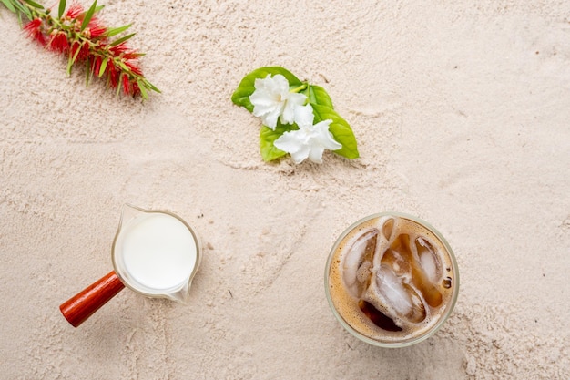 Top view iced coffee, milk and flowers on sand background.