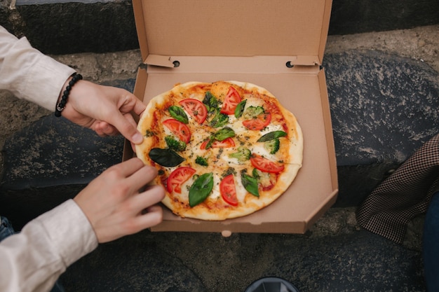 Top view image of couple grab slices of pizza from box at the outdoor